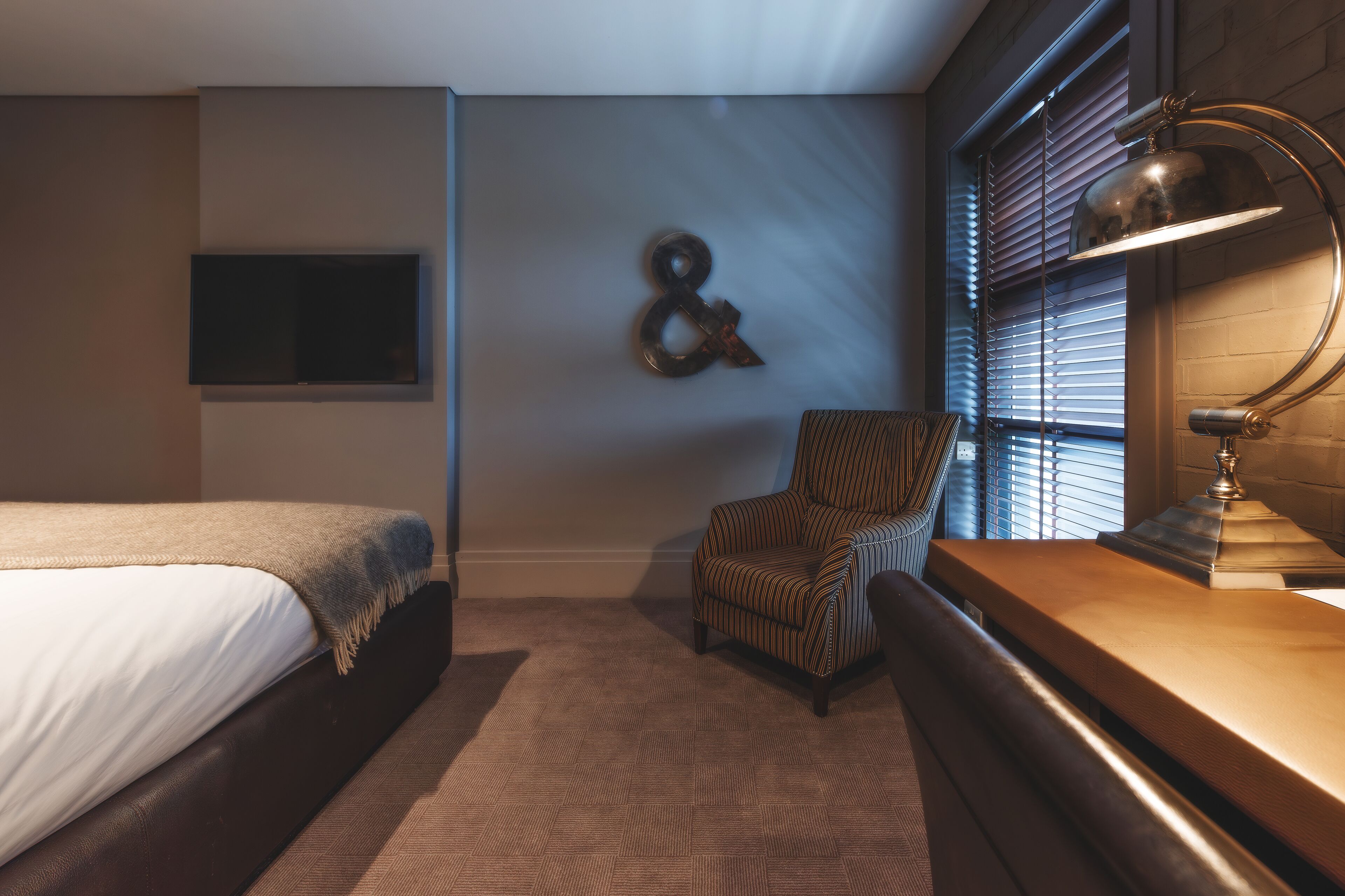 A bedroom with a bed, a chair, a desk, and a lamp.