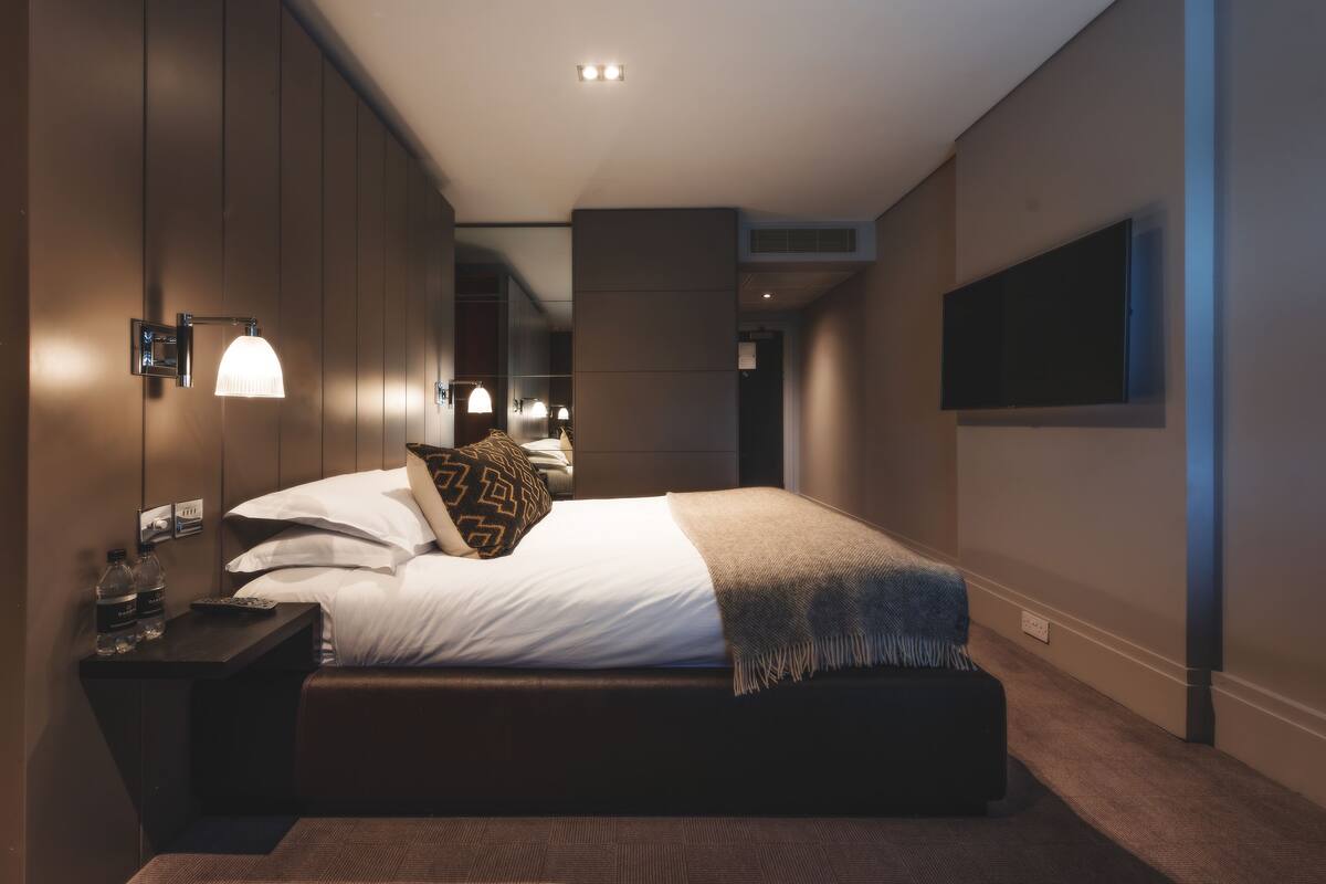 Une chambre d’hôtel moderne avec un grand lit, des lampes de chevet, un téléviseur à écran plat et une petite table avec des bouteilles.