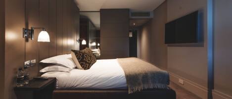 Une chambre d’hôtel moderne avec un grand lit, des lampes de chevet, un téléviseur à écran plat et une petite table avec des bouteilles.