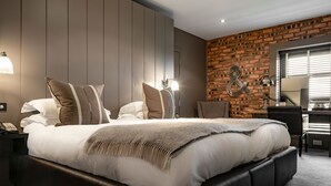 A modern bedroom with a large bed, a brick accent wall, and a desk area. - Dakota Edinburgh (South Queensferry)
