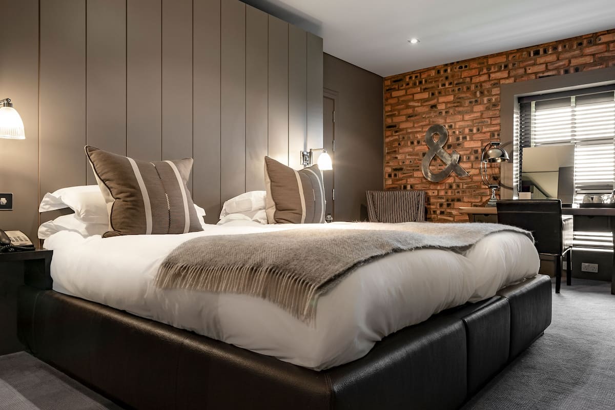 Une chambre moderne avec un grand lit, un mur d’accent en briques et un espace bureau.