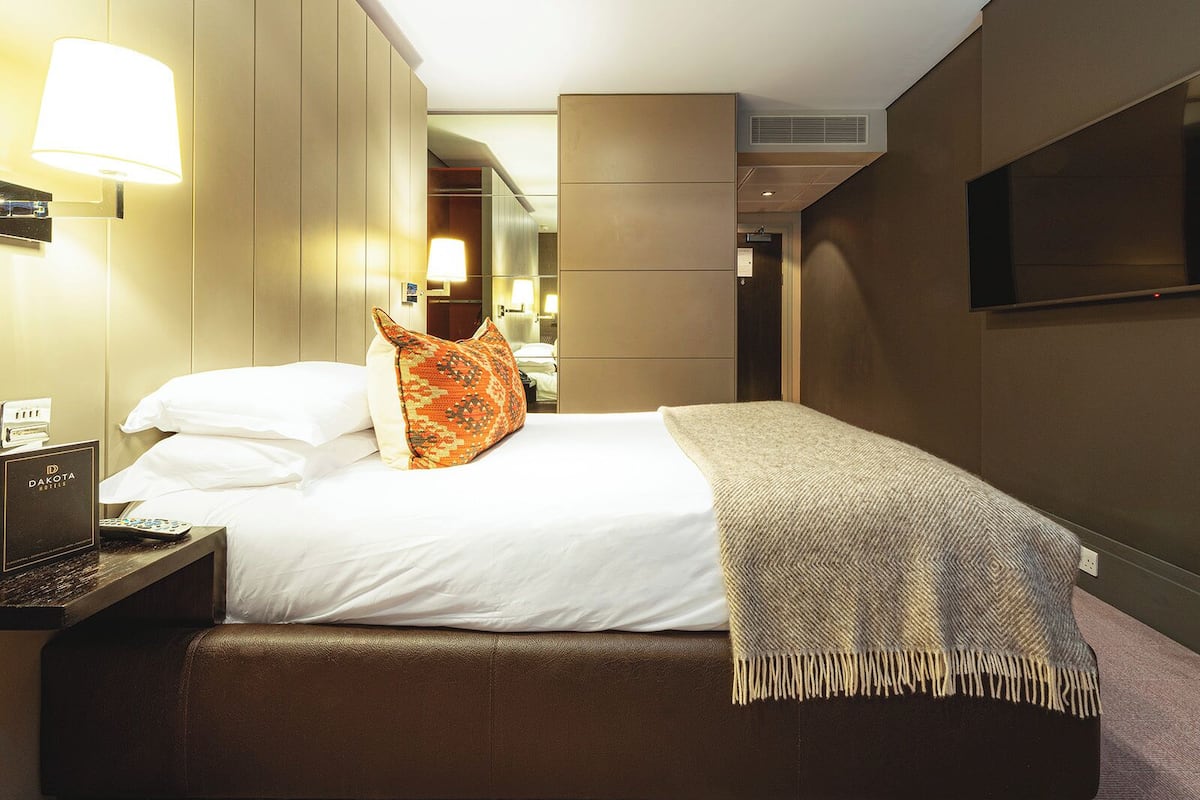 Une chambre d’hôtel équipée d’un lit, d’une lampe de chevet, d’une télévision et d’un bureau avec un téléphone et une télécommande.