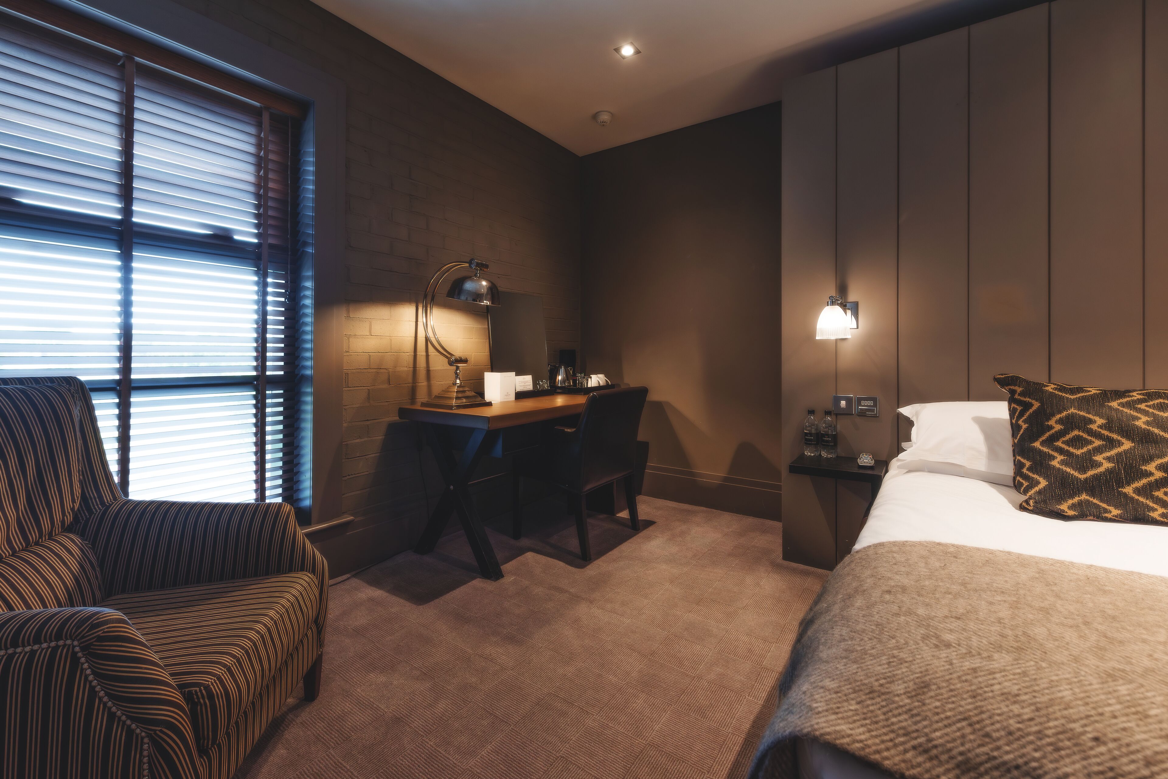 A hotel room with a bed, a desk, a chair, and a nightstand.