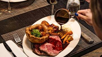 A plate of food including steak, Yorkshire pudding, and vegetables, with a glass of red wine and a water glass on a table.
