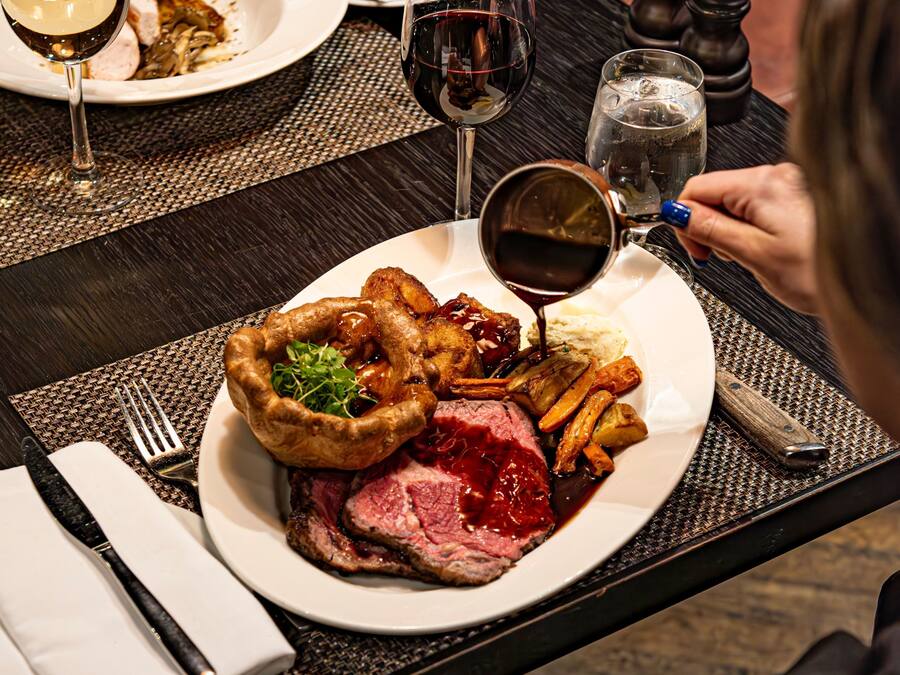 A plate of food including steak, Yorkshire pudding, and vegetables, with a glass of red wine and a water glass on a table.