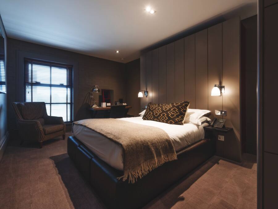 A modern bedroom with a large bed, a chair, bedside tables, and a wardrobe.