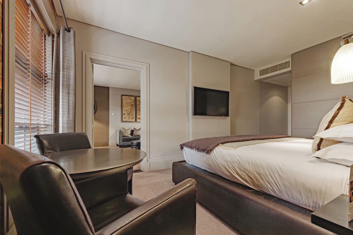 Une chambre d’hôtel équipée d’un lit, d’un bureau, d’une chaise, d’une télévision et d’une fenêtre avec des stores.