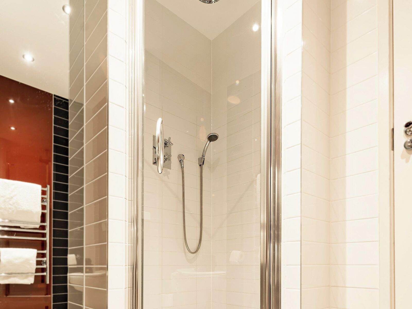 A modern shower with a glass door, chrome fixtures, and a tiled wall.