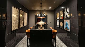 Un comedor moderno con una mesa larga, paredes oscuras y obras de arte enmarcadas.