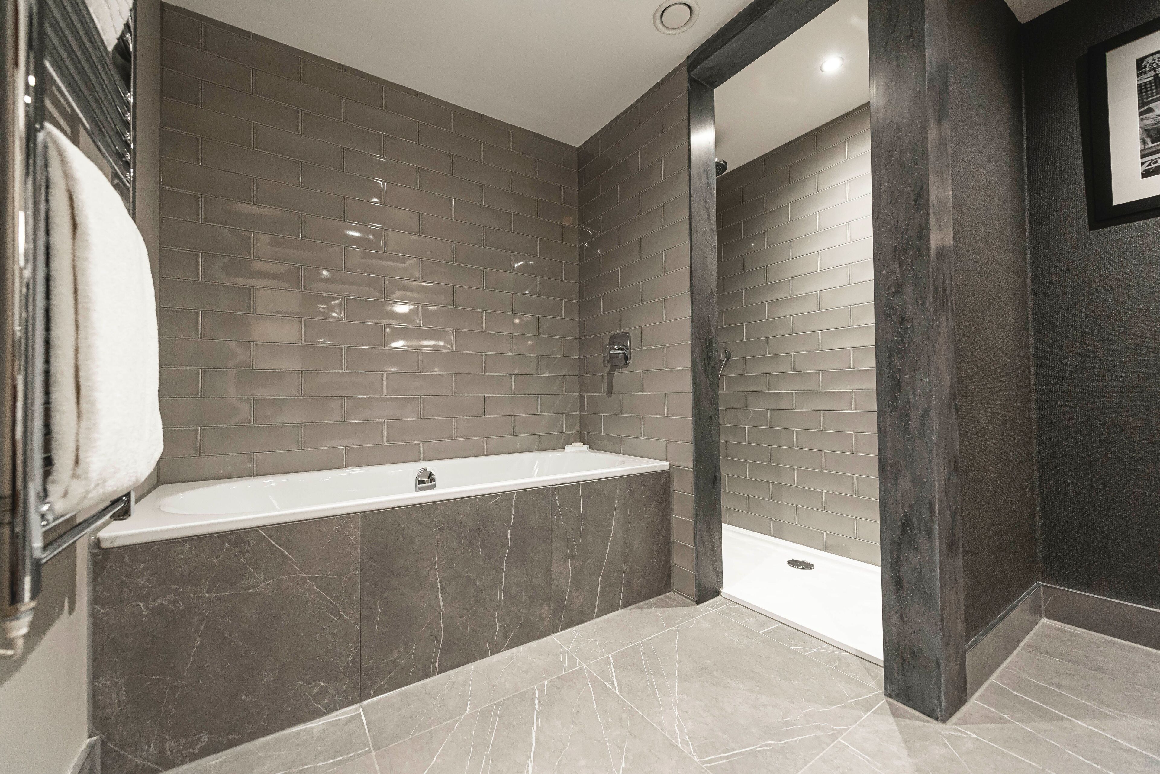 A modern bathroom with a bathtub, shower, and tiled walls.