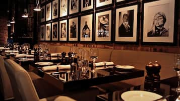 A restaurant with a long table set for dining, framed pictures on the wall, and hanging lights.