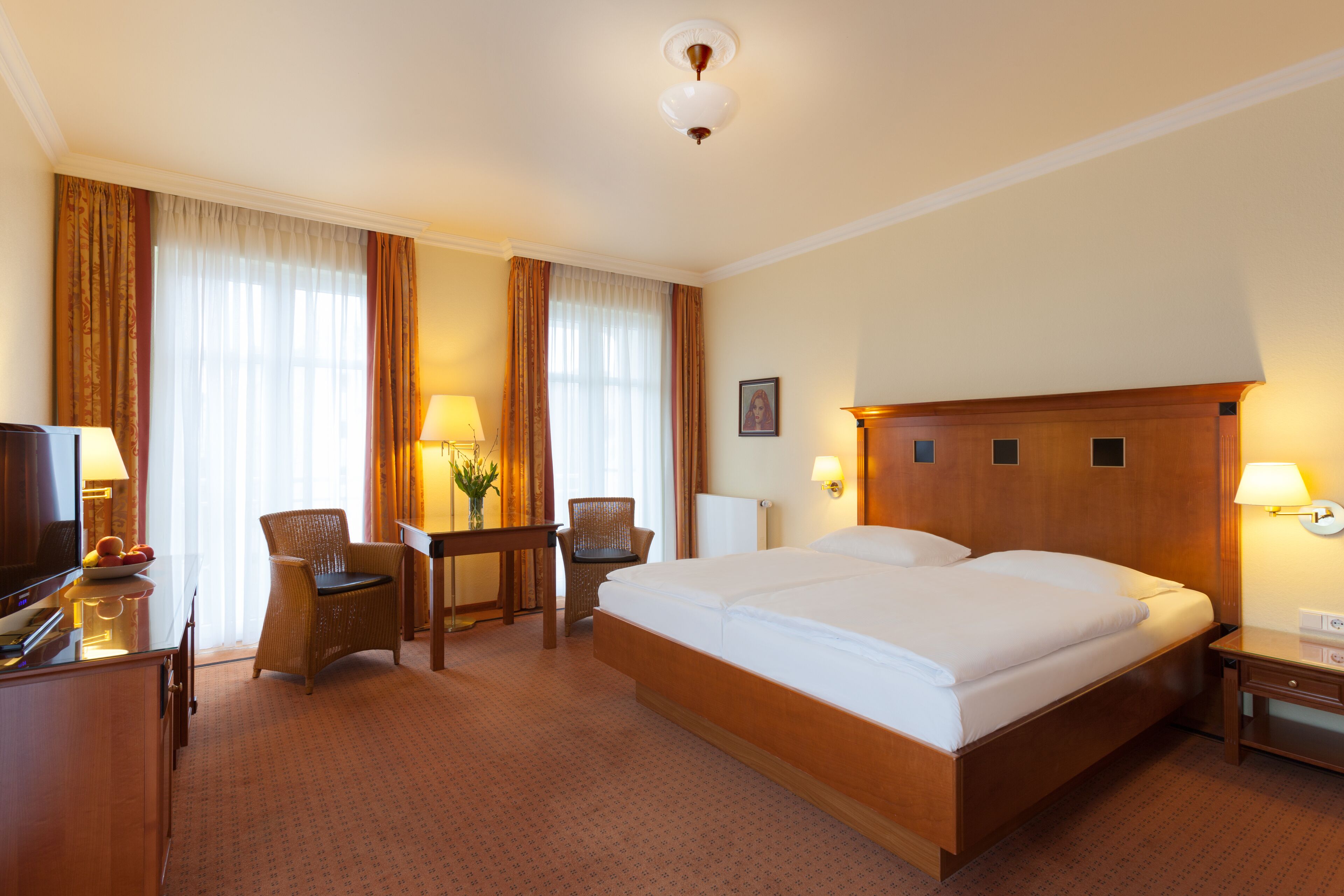 A hotel room with a large bed, a desk with a chair, a television, and a lamp.