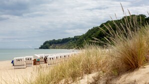 A beach with numbered beach huts and a forested hill in the background. - Vju Hotel Rügen (Göhren)