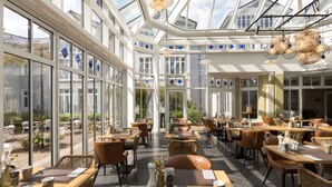 A spacious indoor dining area with large windows, wicker furniture, and a glass ceiling. - Vju Hotel Rügen (Göhren)