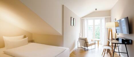 Quarto de hotel com cama, escrivaninha, cadeira e televisão.