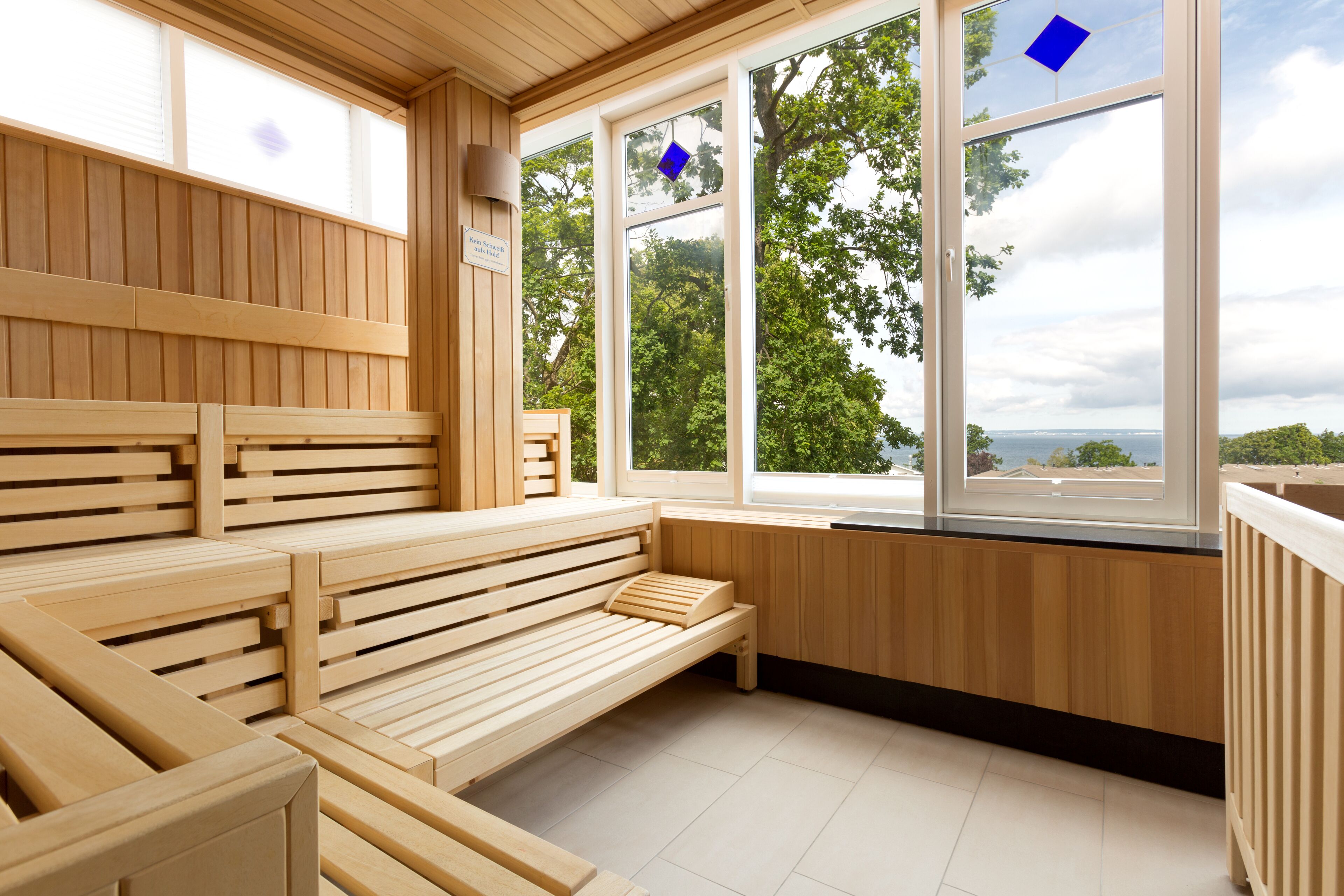 Eine Sauna mit Holzbänken und großen Fenstern, durch die Bäume und Himmel zu sehen sind.