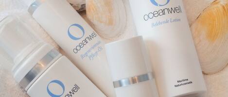 A collection of skincare products from OceanWell, including a moisturizing cream and a skin-lightening cream, arranged on a white towel with seashells.