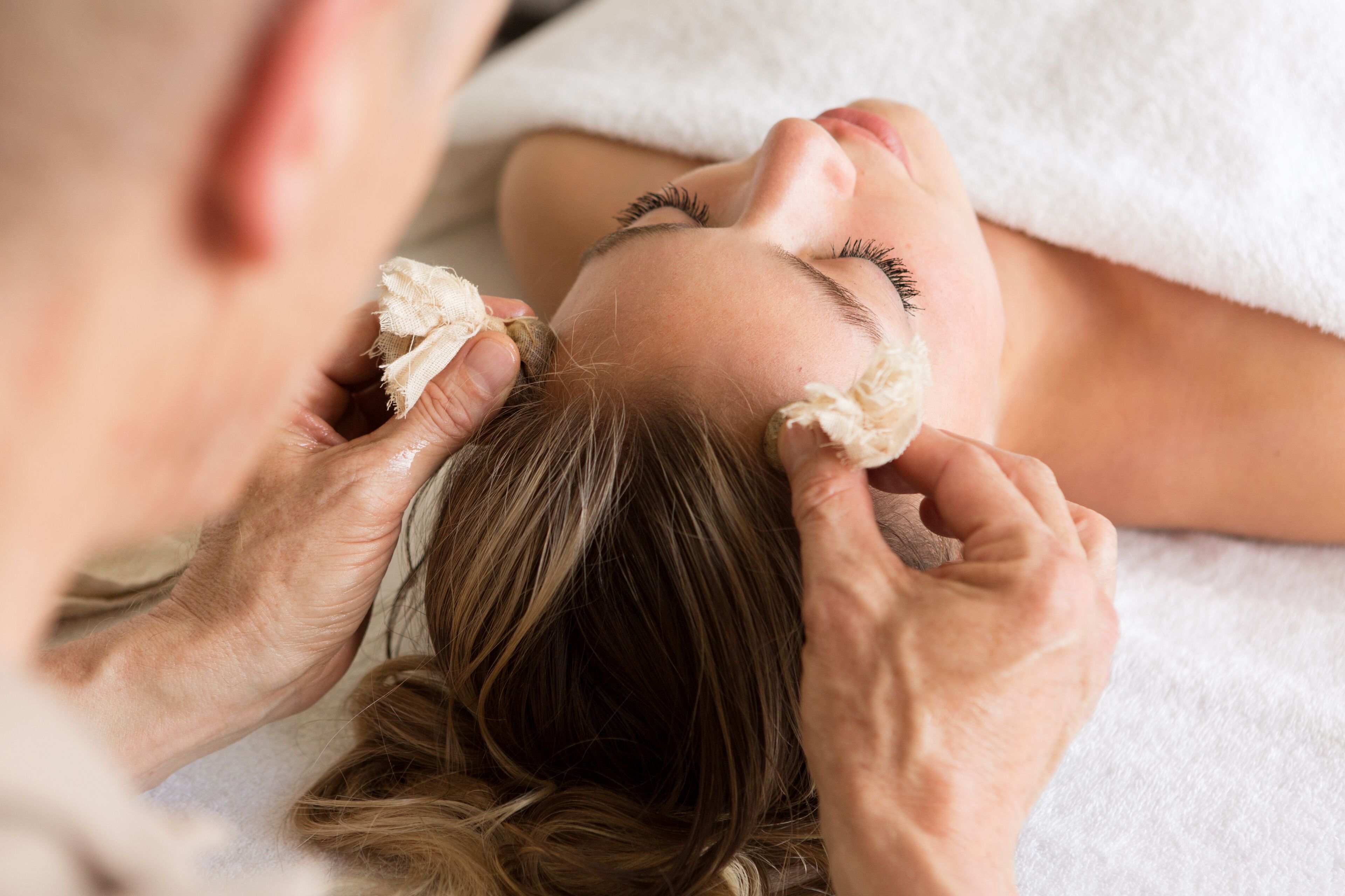 A person receiving a facial treatment with a towel covering their head.