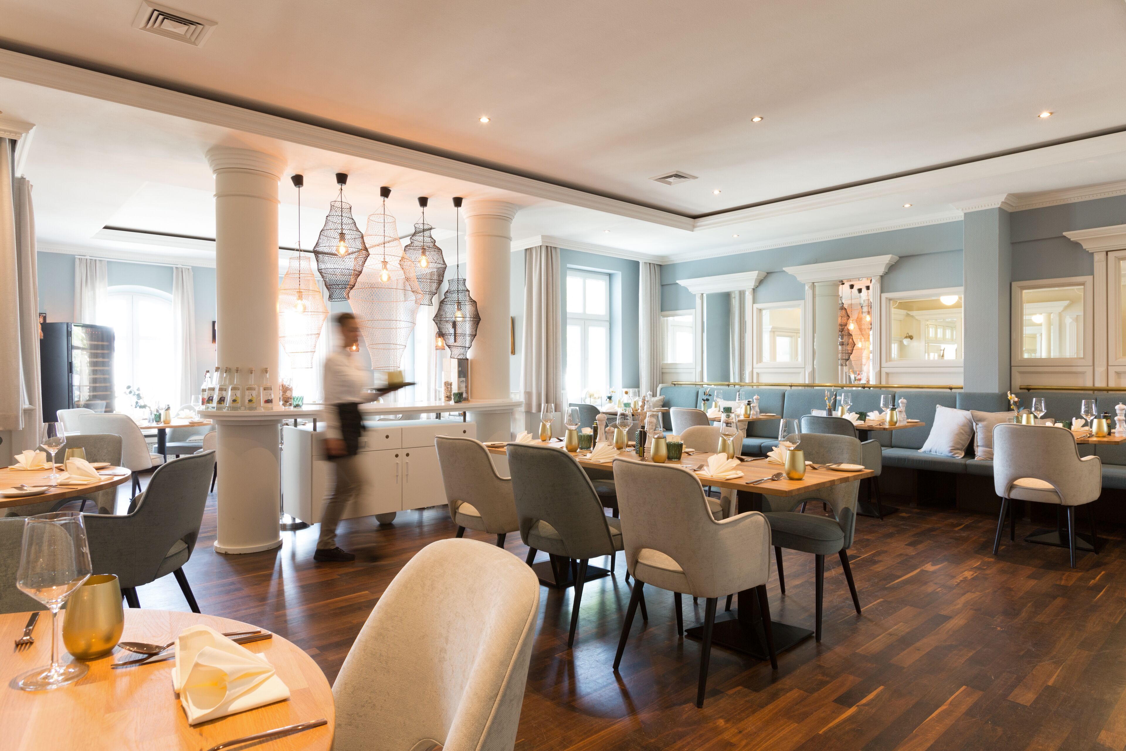 A spacious dining area with multiple tables and chairs, a central column, and hanging pendant lights.