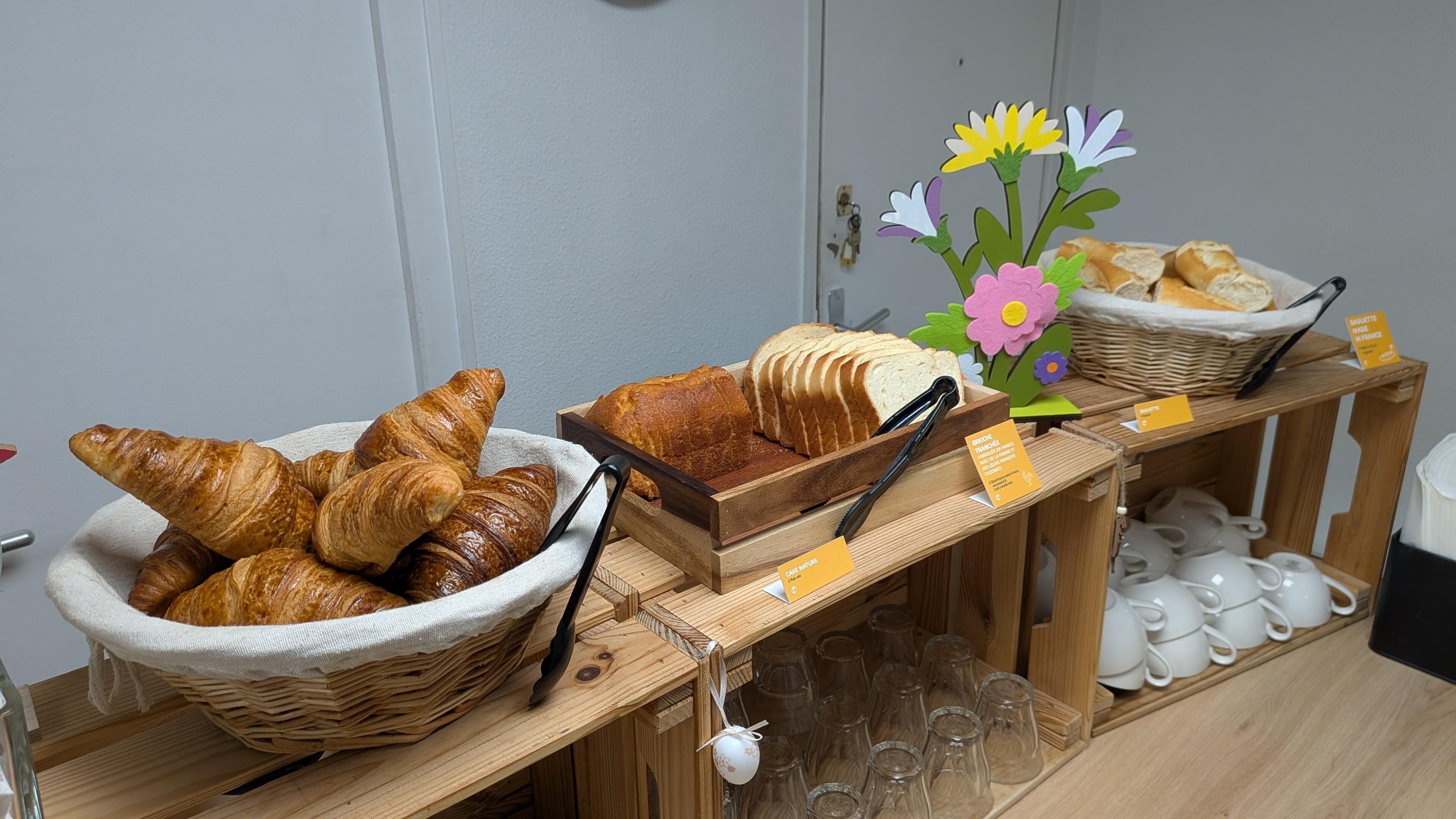En frukostbuffé med croissanter, bröd och en blomsterdekoration.