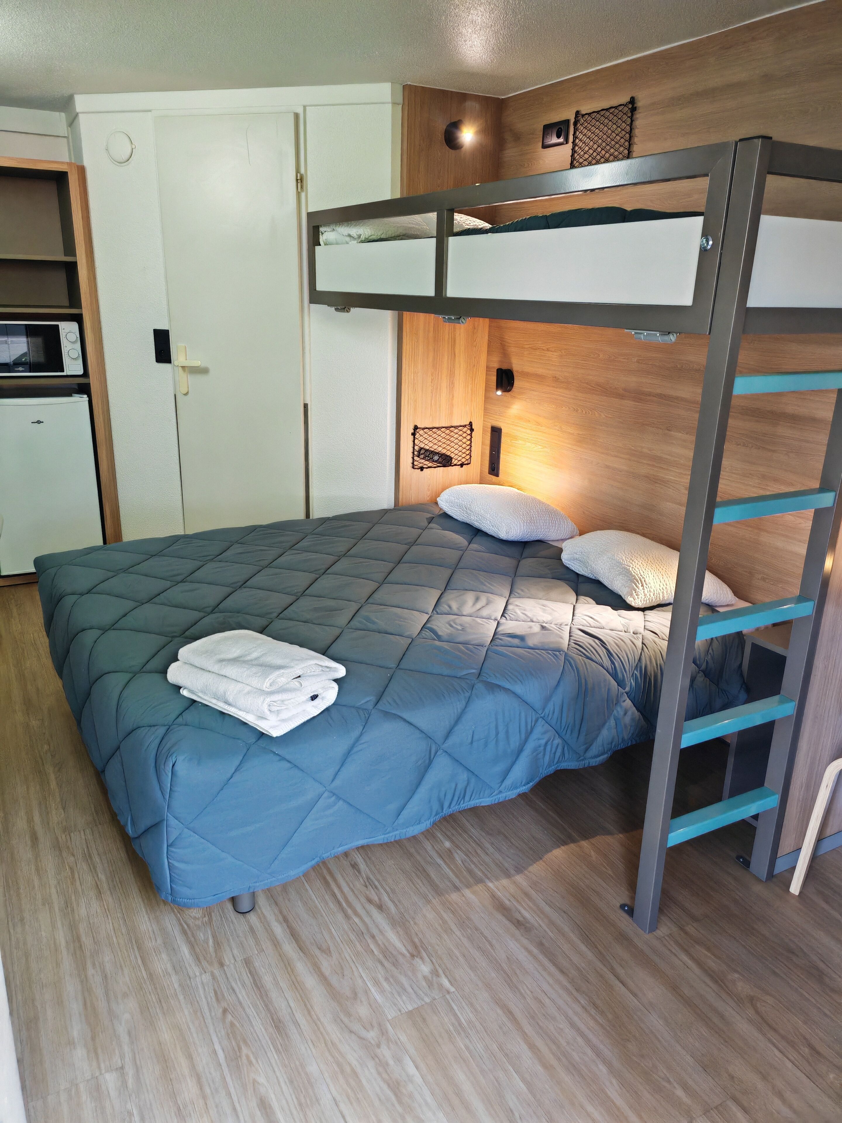 A bunk bed with a blue quilt, a white door, a microwave, and a wooden cabinet.