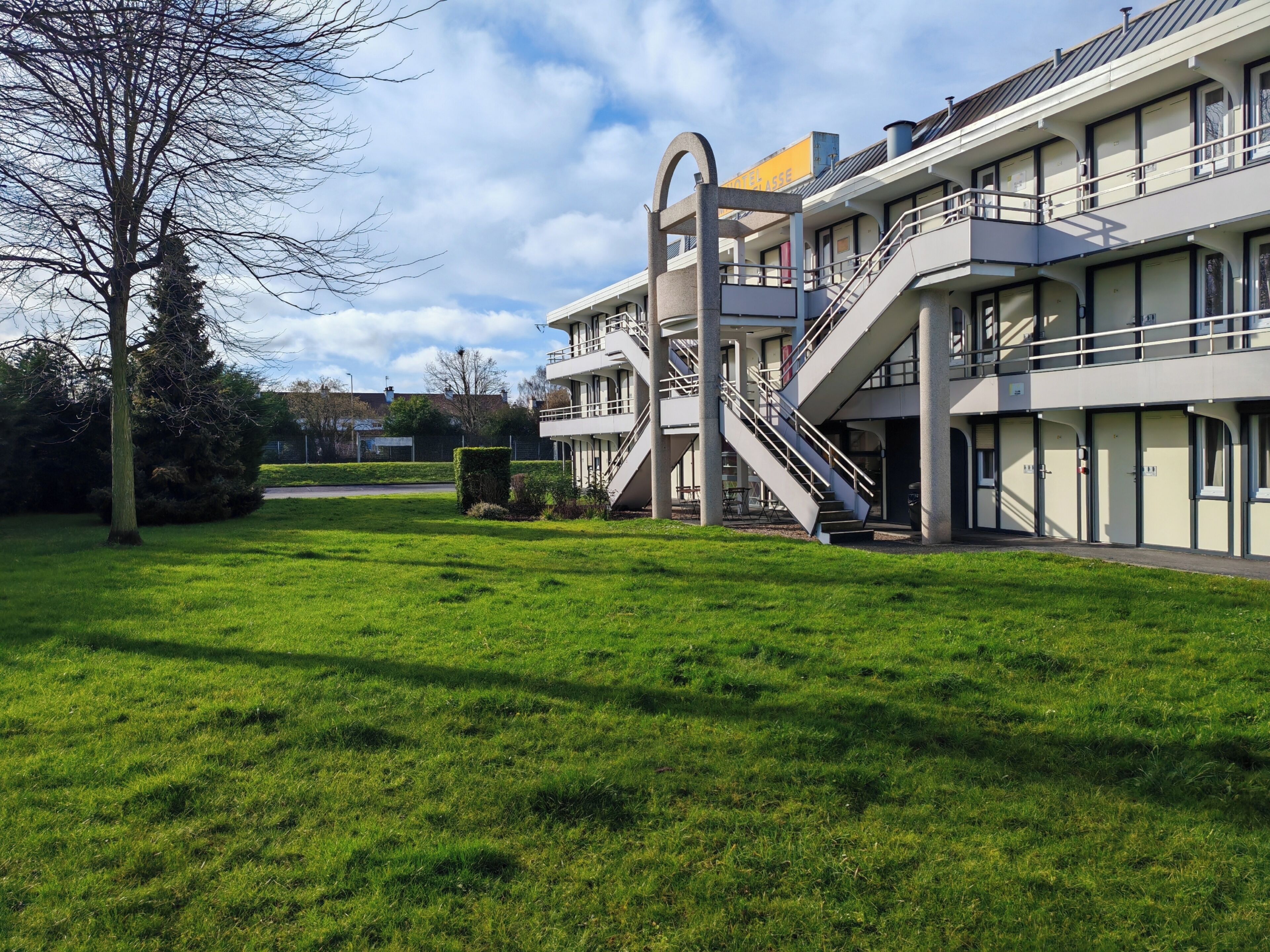 A modern hotel with a central staircase, multiple balconies, and a well-maintained lawn.