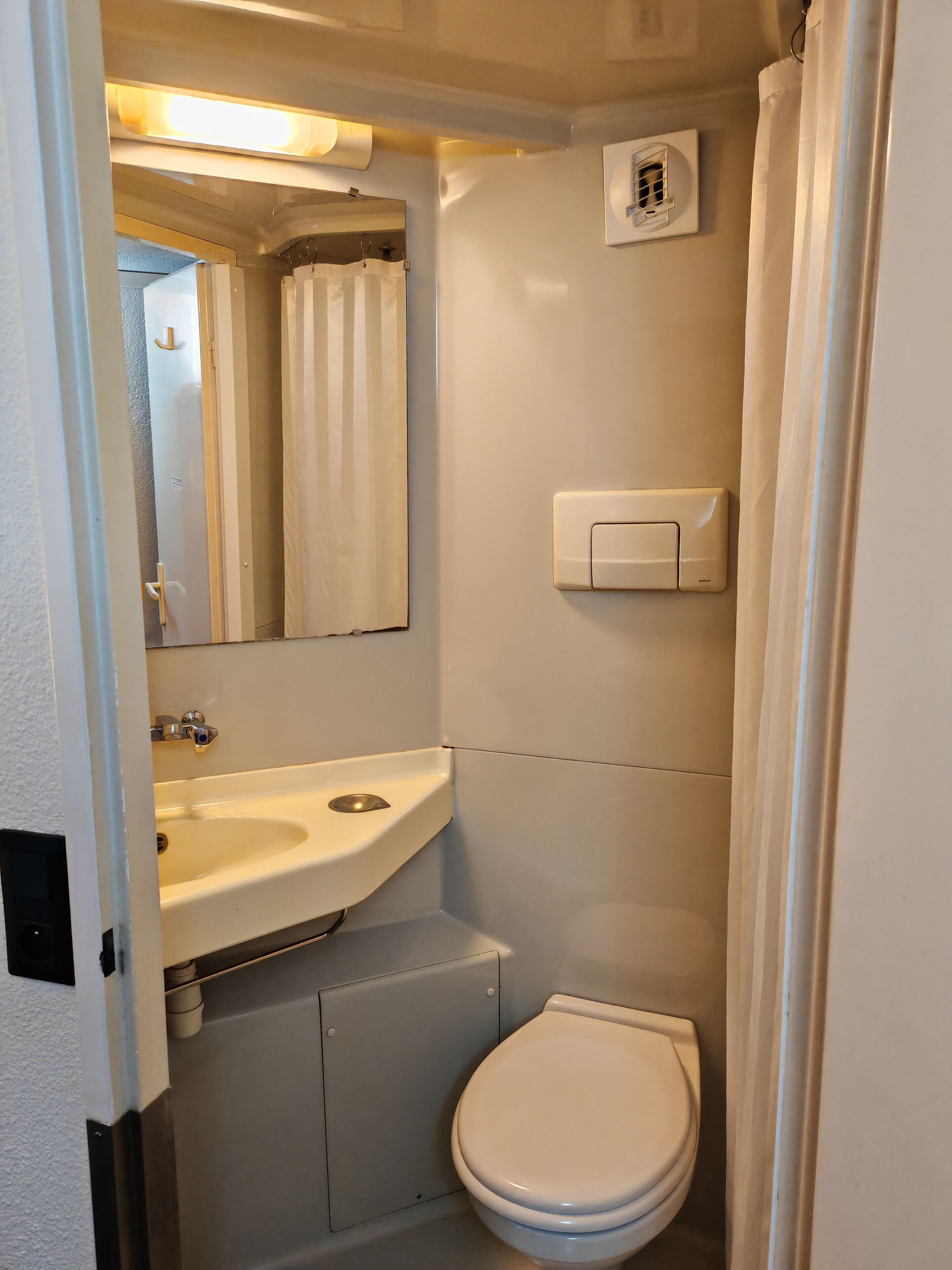 Un baño pequeño y funcional con un lavamanos blanco, un espejo, un inodoro y una cortina de ducha.