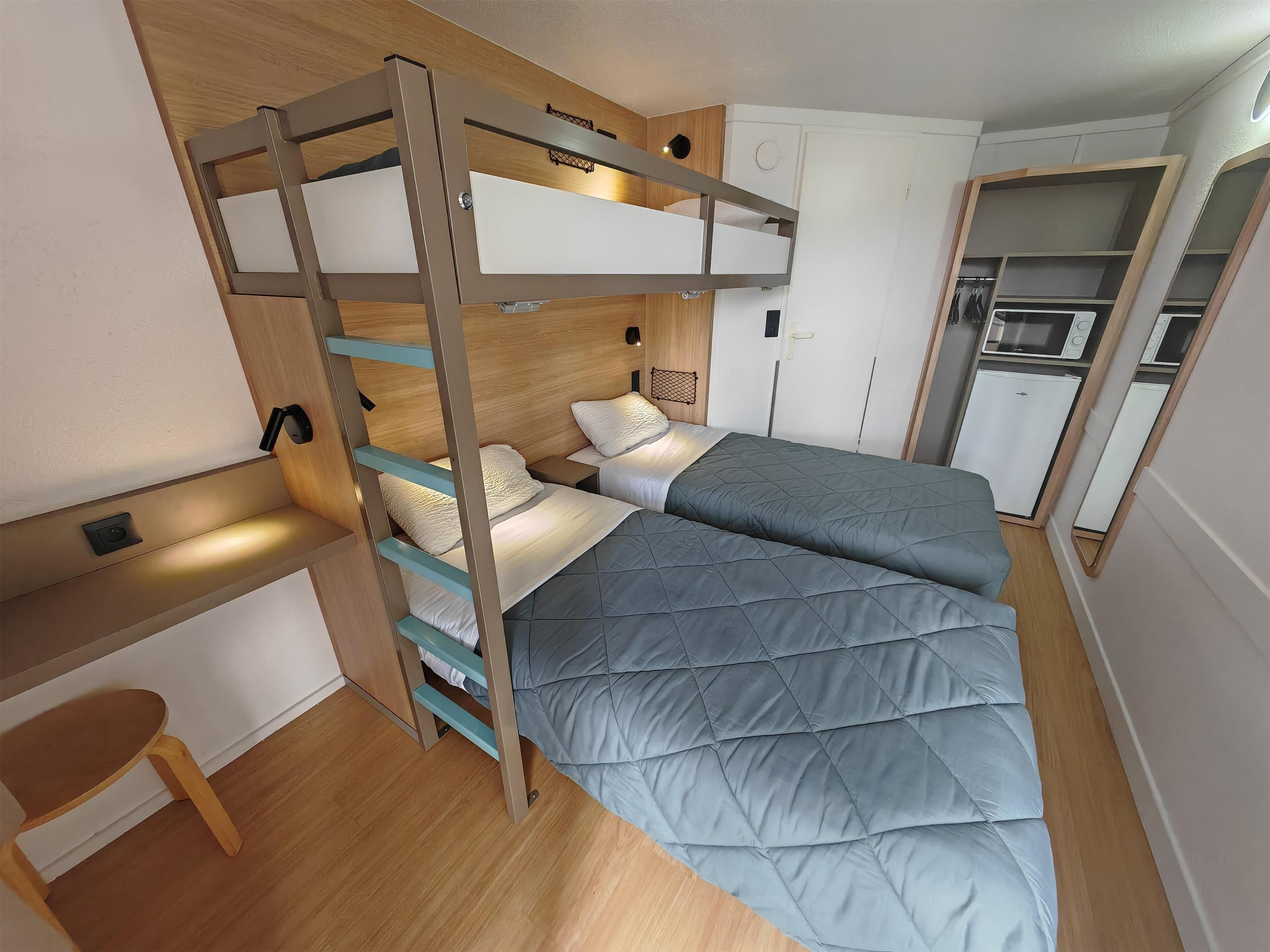 Un dormitorio pequeño con literas, un escritorio y una kitchenette.