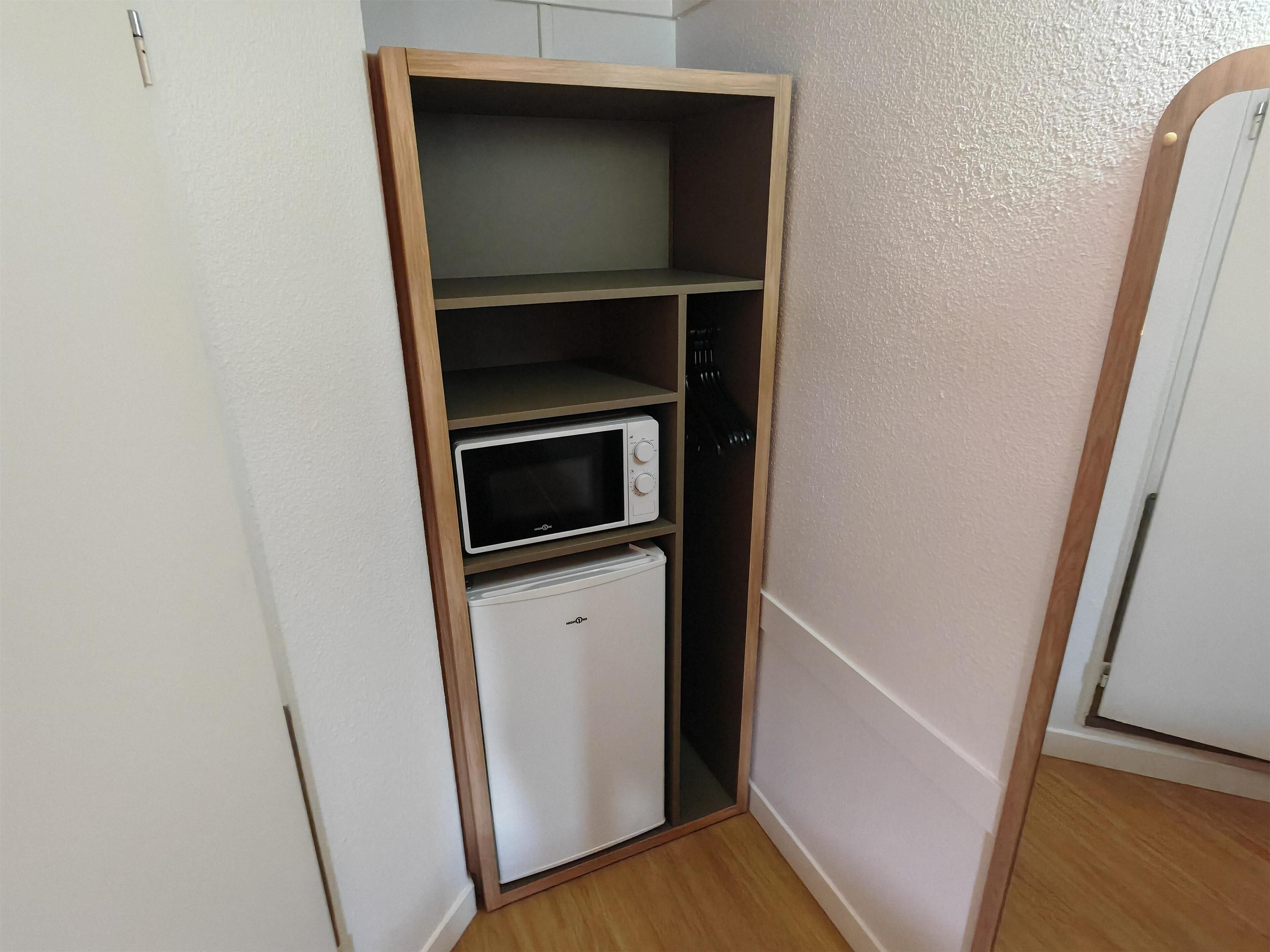 A compact kitchenette with a microwave and a small refrigerator, built into a corner of a room with white walls and wooden flooring.