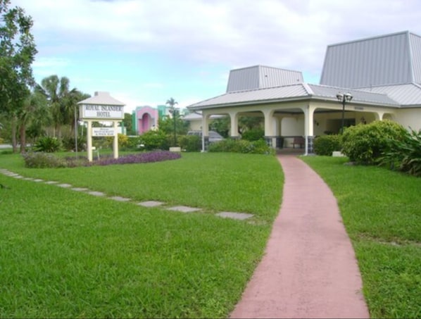 A hotel with a covered walkway, lush green lawn, and a sign indicating it is a Royal Islander Hotel.