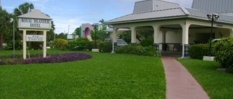 The Royal Islander Hotel with a covered outdoor seating area, a pathway leading to the entrance, and a landscaped garden with purple flowers.