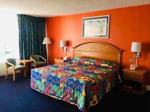 A hotel room with a large bed, two bedside tables with lamps, a chair, and a window with curtains. - Royal Islander Hotel (Freeport)