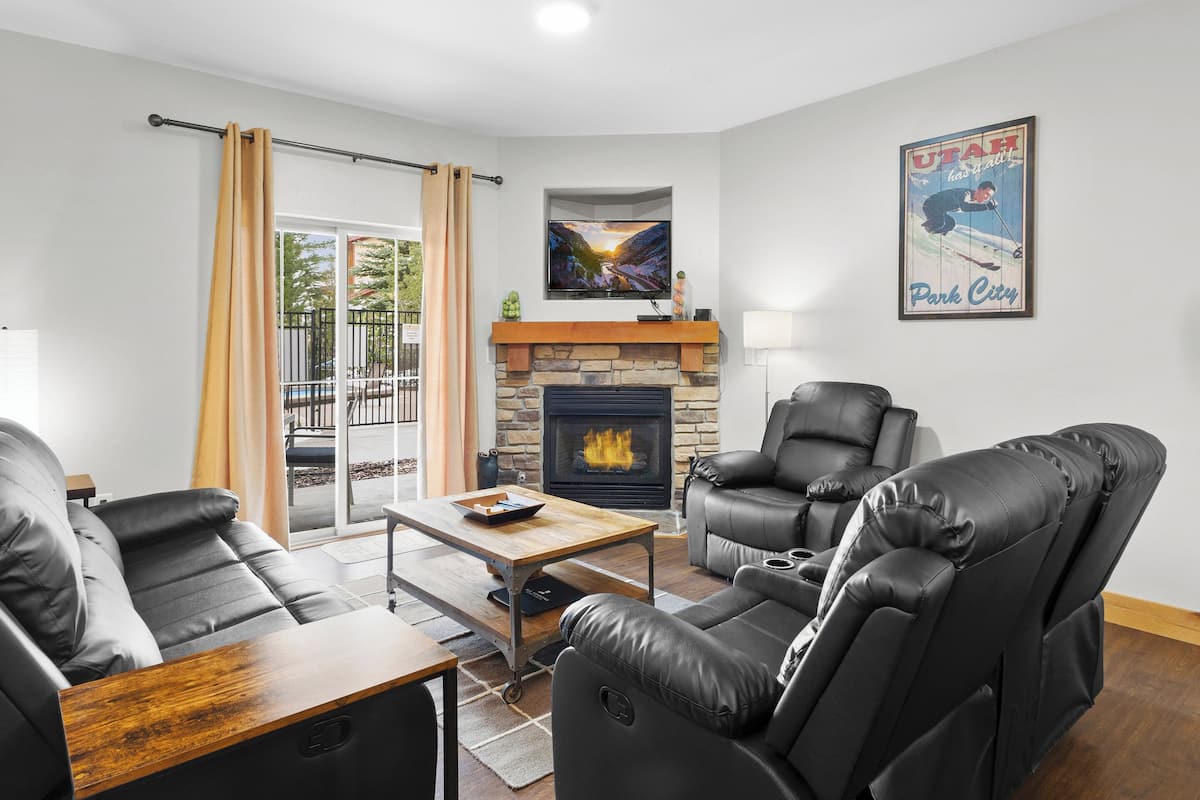 A modern living room with leather sofas, a fireplace, a mounted TV, and a poster on the wall.