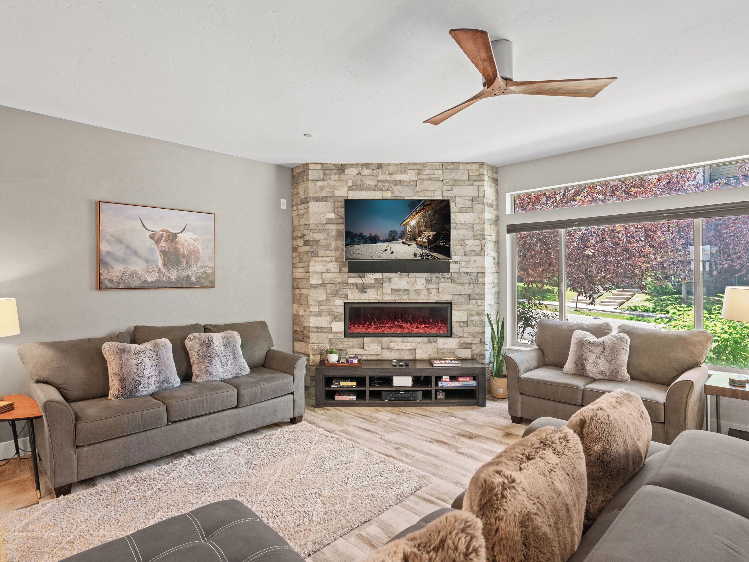 A modern living room with a stone fireplace, a mounted TV, and a ceiling fan.