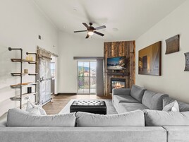 A spacious living room with a grey sofa, a fireplace, a mounted TV, and a ceiling fan.