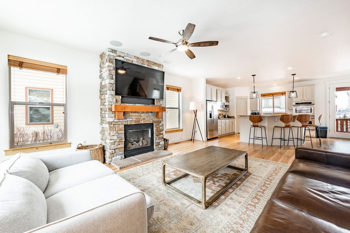 A modern living room with a fireplace, a large TV, and a ceiling fan.