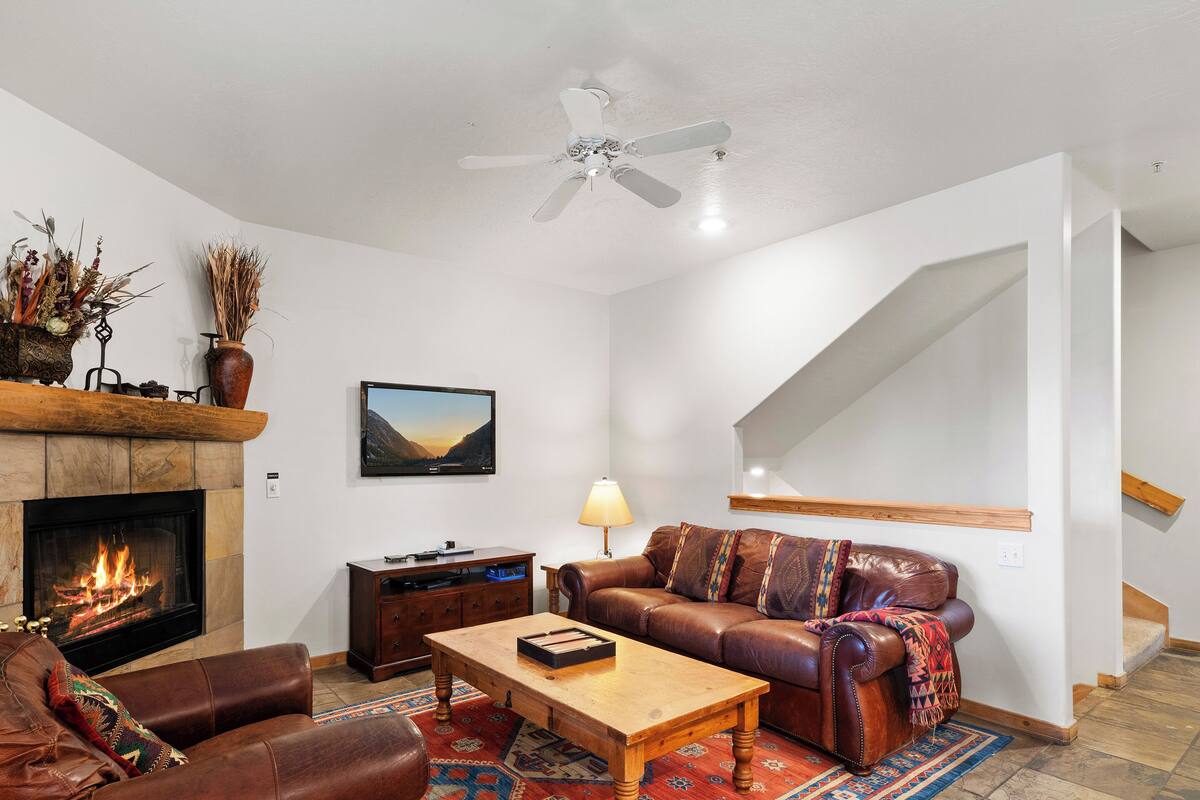 A living room with a fireplace, leather sofa, coffee table, and a television on the wall.