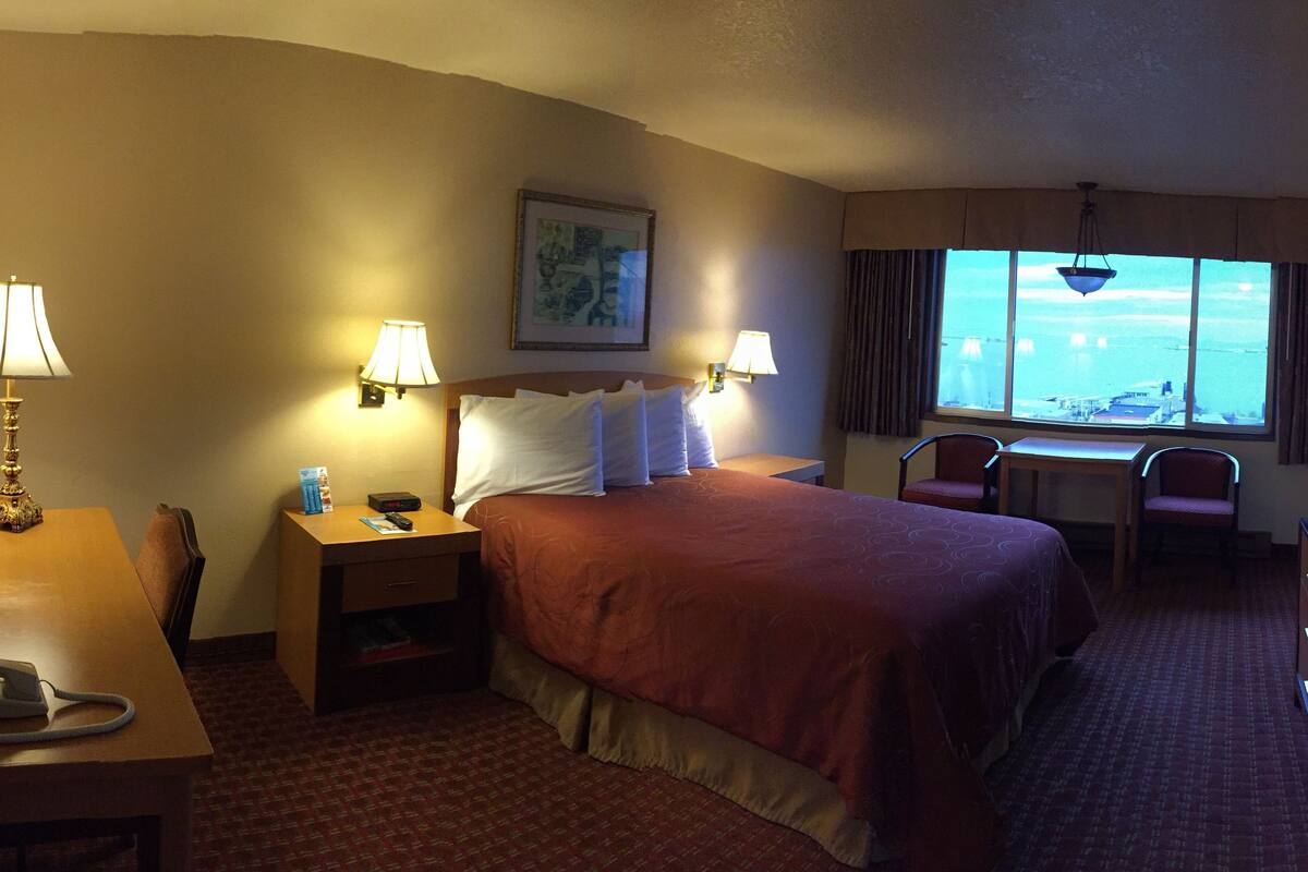 A hotel room with a bed, bedside lamps, a desk with a telephone, a chair, a television, and a window with a view.