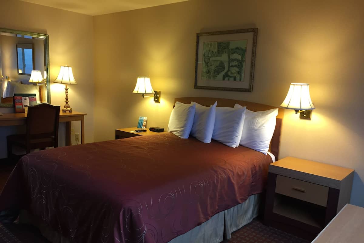 A hotel room with a large bed, two bedside tables with lamps, a desk with a chair, and a framed picture on the wall.