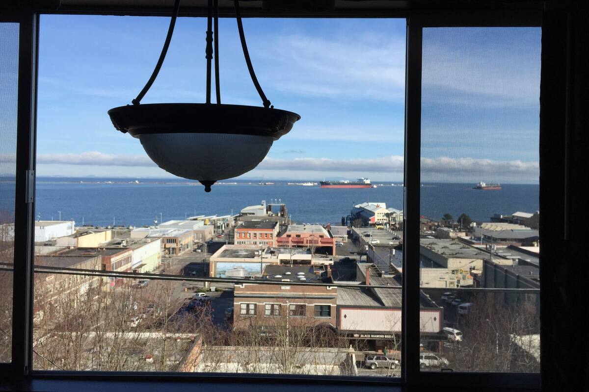 A view from a window overlooking a coastal industrial area with ships in the distance.