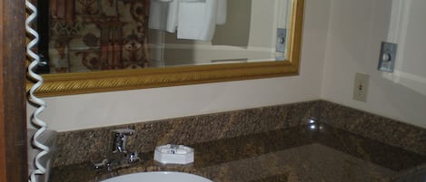 Een badkamer met een granieten aanrechtblad, een wit wastafelmeubel, een spiegel met gouden lijst en een handdoekrek met witte handdoeken.