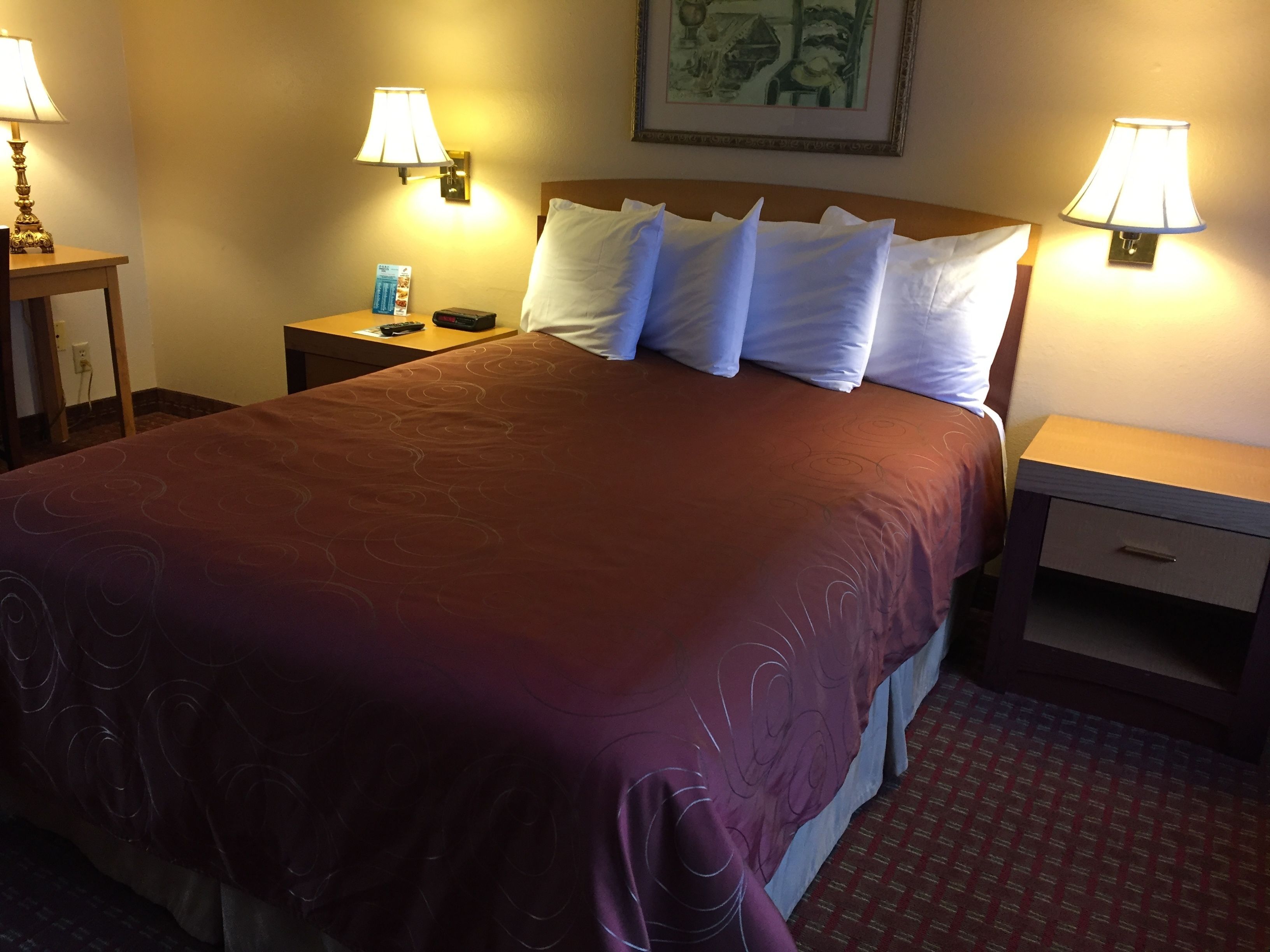 A hotel room with a large bed, two bedside tables, and two wall-mounted lamps.