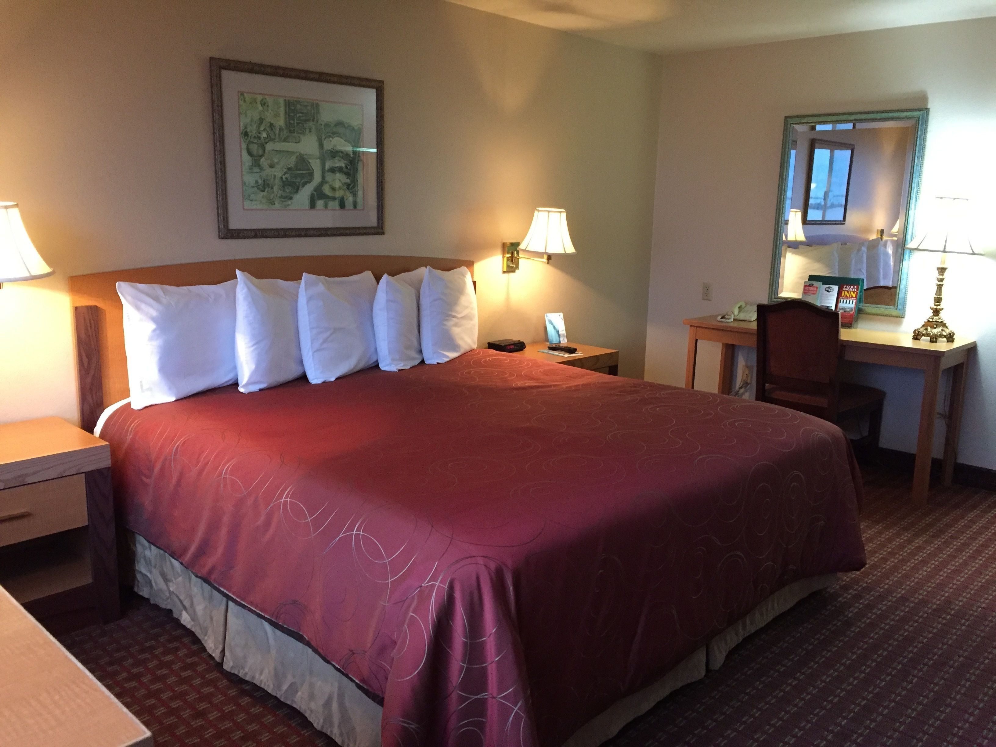 Una habitación de hotel con una cama grande, dos mesitas de noche, un escritorio, una silla y un espejo.
