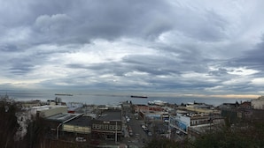 A coastal town with a mix of commercial and residential buildings, a busy street, and a large body of water with ships in the distance.