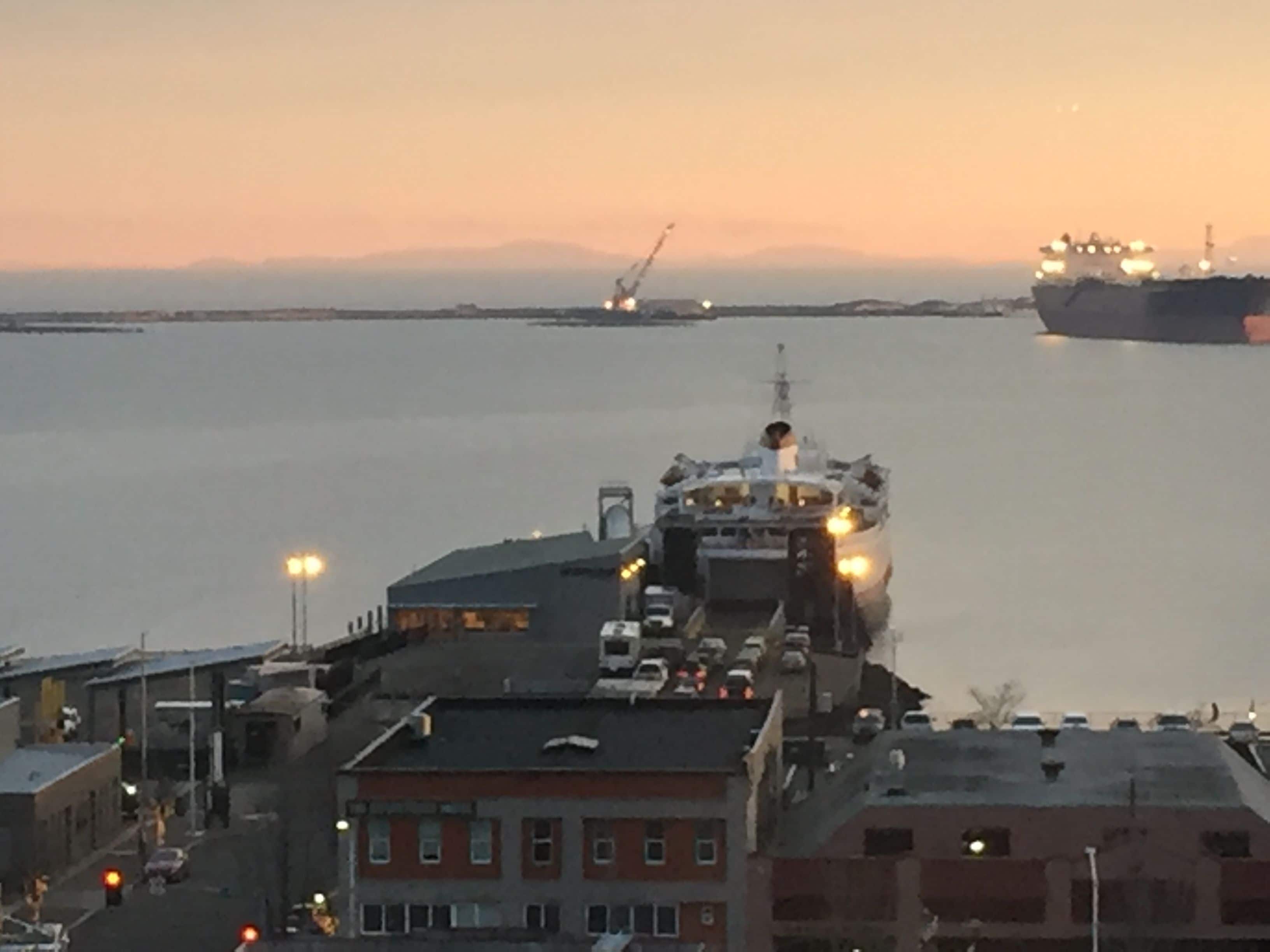 A large ship docked at a port with a cityscape in the background.