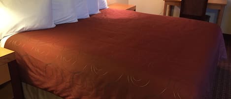 A hotel room with a large bed, a nightstand, a lamp, and a small table with a chair.