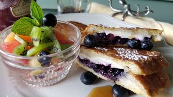 A dessert plate with a fruit salad, a slice of blueberry cake, and a small pitcher of syrup.