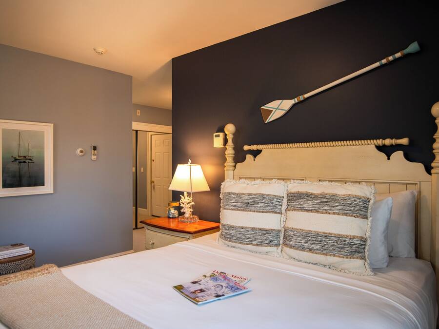 A neatly made bed with a magazine, a bedside lamp, and a framed picture on the wall.