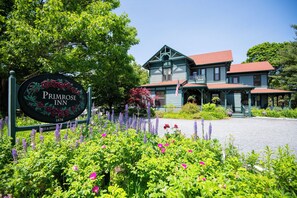 A historic building with a sign reading "Primrose Inn 1878" surrounded by lush gardens and purple flowers. - The Primrose (Bar Harbor)