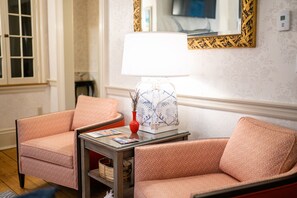 A room with two matching armchairs, a small table with a lamp, and a mirror on the wall.